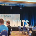 Giant letters on stage that say N M T S. The backdrop says New Mexico Tech Summit